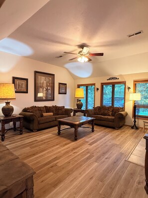 A living room with a ceiling fan, wooden flooring, and two couches.
