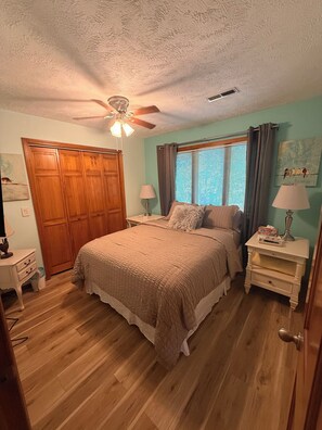 A bedroom with a bed, nightstands, a ceiling fan, a window with curtains, and a wooden wardrobe. - Guest house, convenient setting, large wooded lot of towering oaks (Hollister)