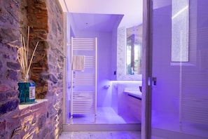 A bathroom with a stone wall, a white towel rack, a glass shower enclosure, and a mirror.