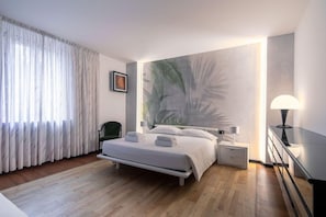A bedroom with a bed, bedside table, lamp, and a large wall painting.