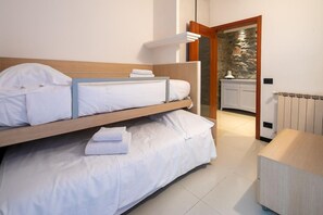 A bedroom with a bunk bed, a bedside table, a radiator, and a view of a stone wall through an open door. - Ponte Rosso Modern (Florence)