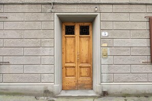 A double wooden door with a brass plaque, set in a stone wall with a number plate. - Ponte Rosso Modern (Florence)