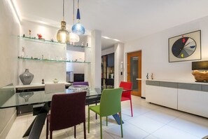 A modern dining area with a glass table, colorful chairs, and decorative items on shelves. - Ponte Rosso Modern (Florence)