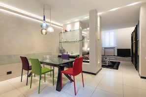 A modern dining area with a glass table, colorful chairs, and a glass shelving unit with decorative items.