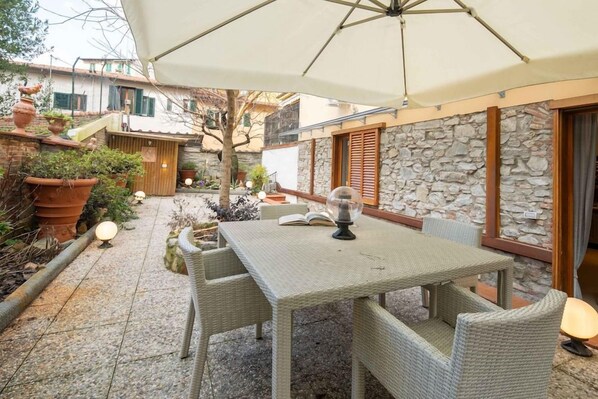 An outdoor patio with a table and chairs, surrounded by potted plants and a stone wall.