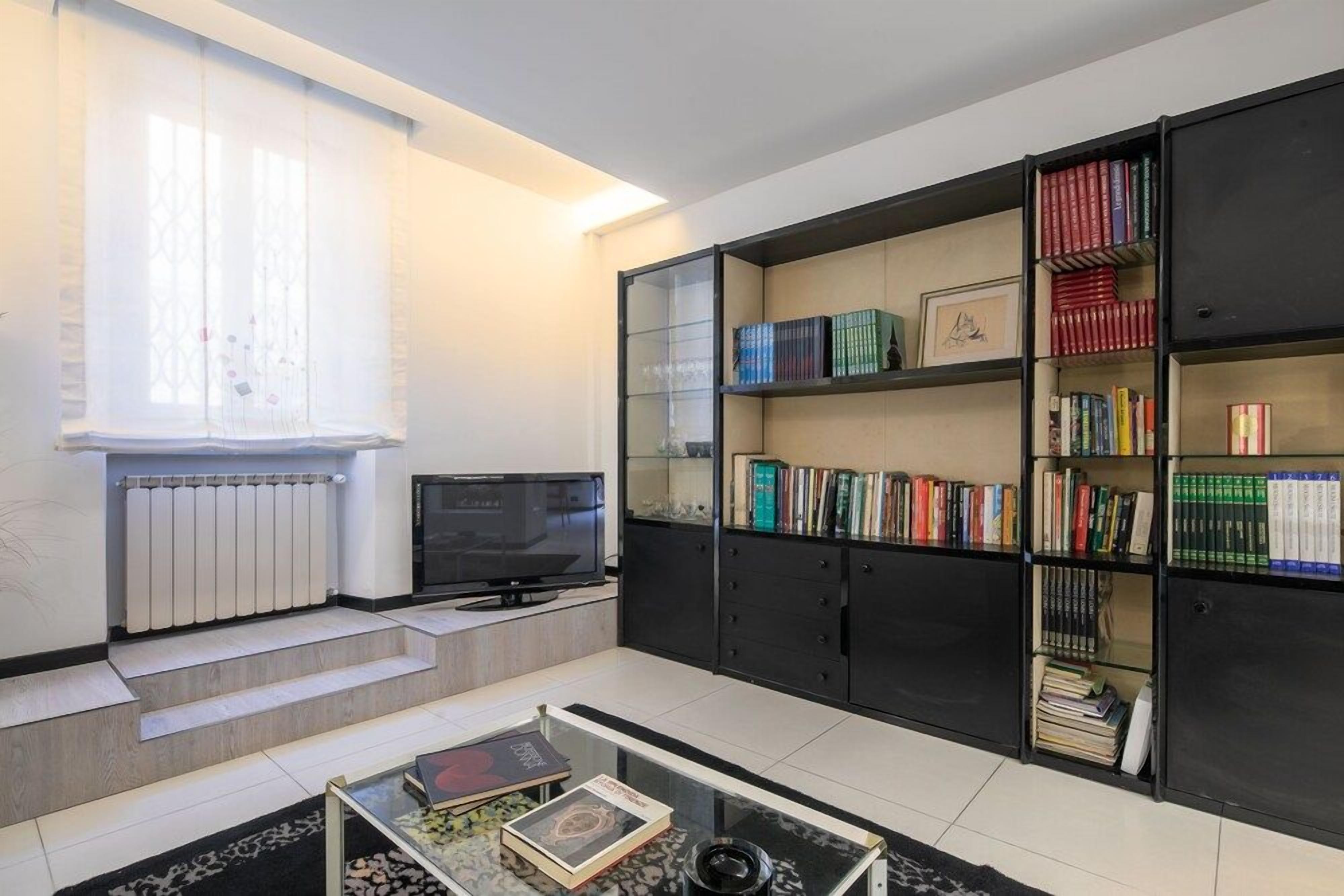 A modern living room with a flat-screen TV, a bookshelf, and a coffee table.