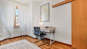Et værelse med trægulv, et skrivebord med stol, en radiator, et vindue med gardiner og et kort på væggen.