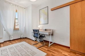 Ein Zimmer mit Holzboden, einem Schreibtisch mit Stuhl, einem Heizkörper, einem Fenster mit Vorhängen und einer Karte an der Wand.