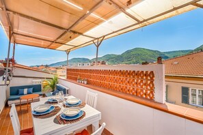 A terrace with a table set for dining, a sofa, and a view of the city and hills. - [GoodTimes] Near the station-5Terre-A/C (La Spezia)