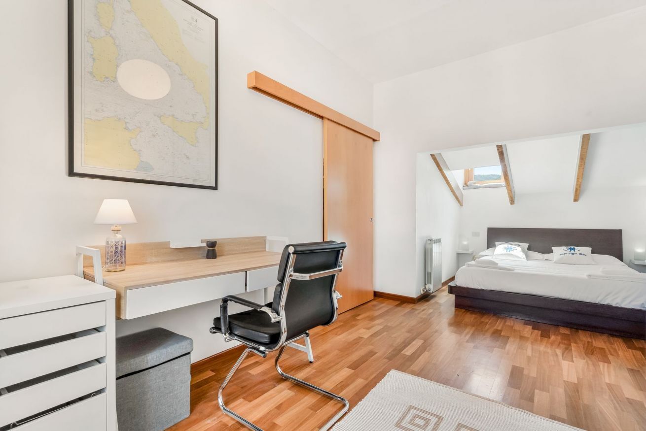 Une chambre d’hôtel moderne avec un plancher en bois, un bureau avec une chaise, un lit, un grand miroir et une carte accrochée au mur.