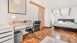 Et moderne hotelværelse med trægulv, et skrivebord med stol, en seng, et stort spejl og et kort på væggen.
