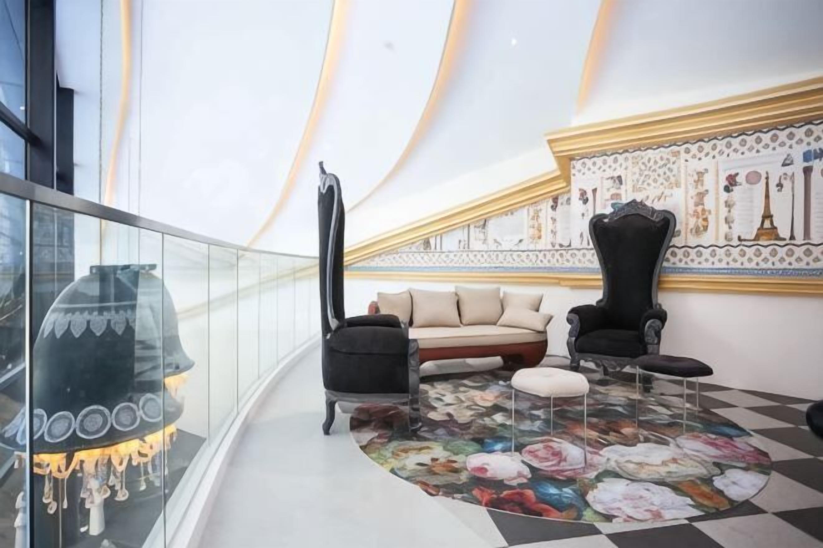 A balcony with a glass railing, a sofa, two armchairs, and a patterned floor.