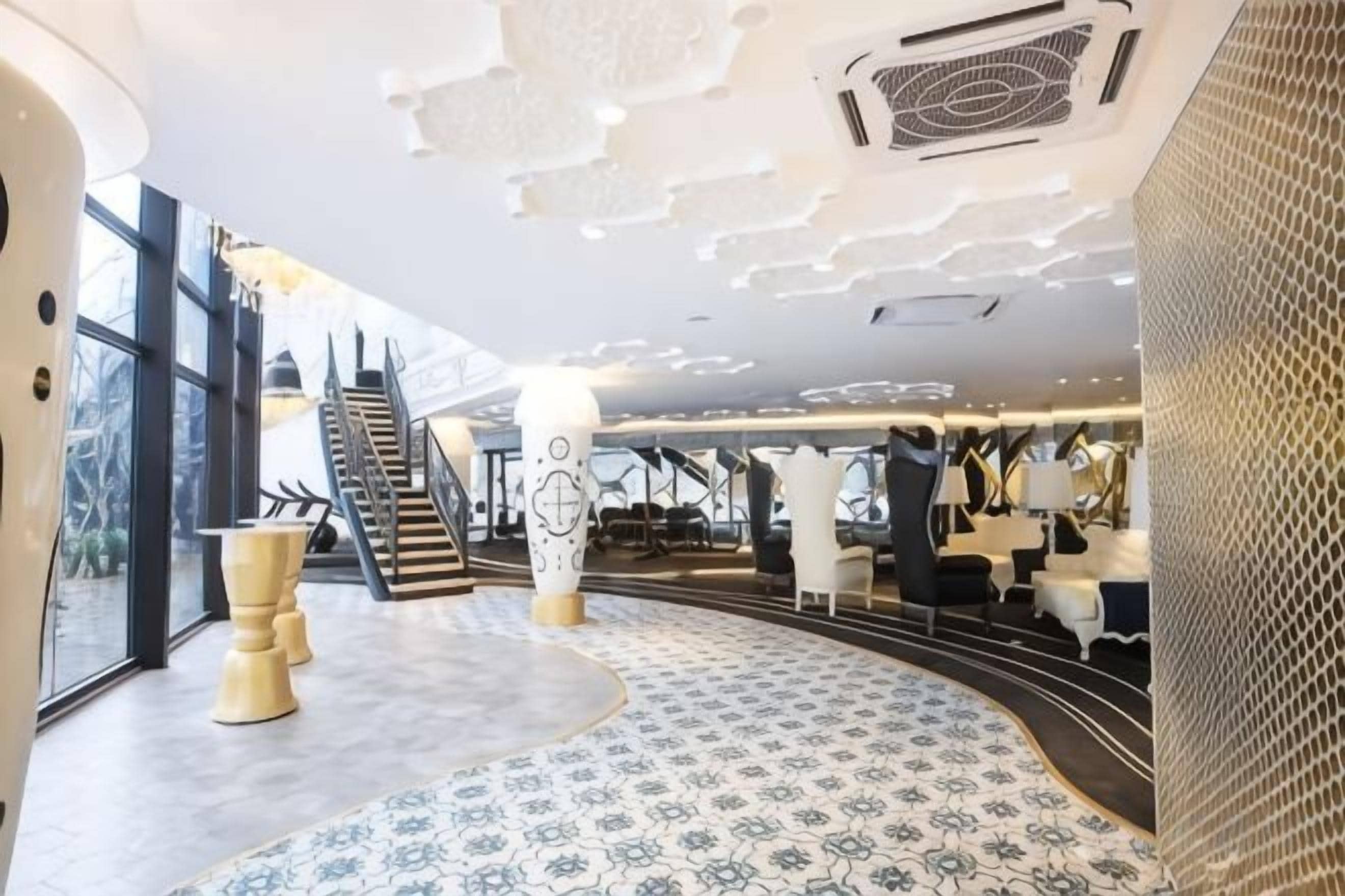 A modern hotel lobby with a curved seating area, a staircase, and a view of the outdoors.