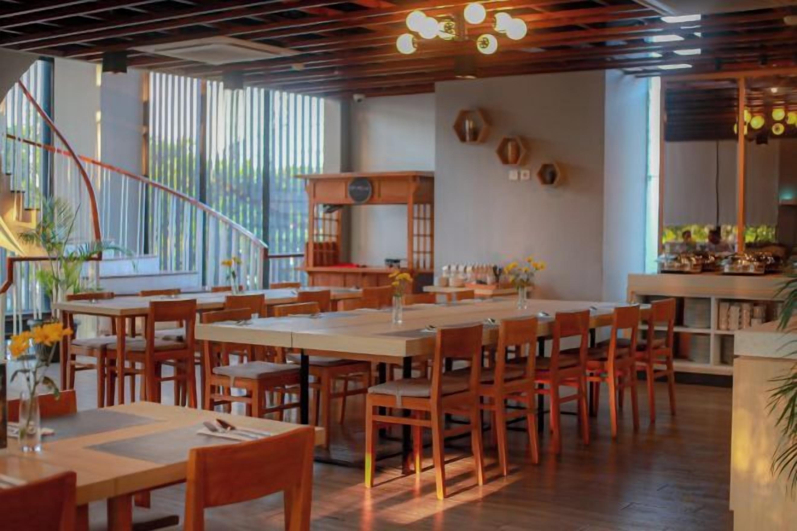 A restaurant with wooden tables and chairs, a staircase, and a kitchen area.