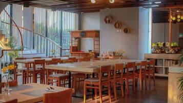 A restaurant with wooden tables and chairs, a staircase, and a kitchen area.