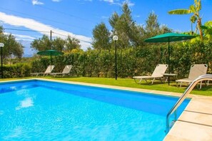 A swimming pool with lounge chairs and umbrellas, surrounded by greenery. - Villa Giannis (Apokoronas)