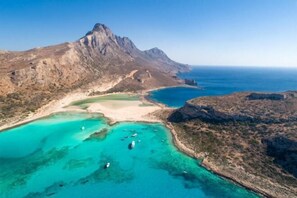 Luftaufnahme einer Küstenlandschaft mit einem Berg, klarem türkisblauem Wasser und Booten.