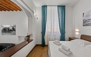 A hotel room with a bed, a wooden headboard, a nightstand, a wall-mounted lamp, and a window with curtains. - Balconcini de Saracini Villa (Siena)