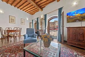 Ein Wohnzimmer mit blauem Sessel, Glastisch, gemustertem Teppich, Holzmöbeln und einem Stadtbild.