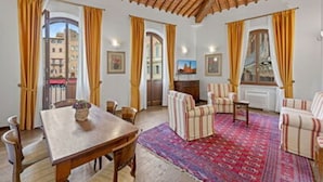 Ein geräumiges Wohnzimmer mit Holzboden, einem Esstisch, gestreiften Sesseln und einem gemusterten Teppich.