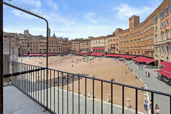 A plaza with a central open space surrounded by buildings with red awnings, a clear sky, and a metal railing in the foreground. - Balconcini de Saracini Villa (Siena)