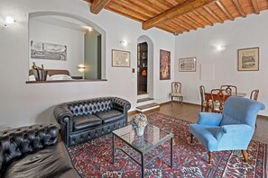 A living room with a black leather sofa, a blue armchair, a glass coffee table, and a patterned rug. - Balconcini de Saracini Villa (Siena)