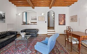 A living room with a sofa, armchair, coffee table, and a dining area with chairs and a table. - Balconcini de Saracini Villa (Siena)