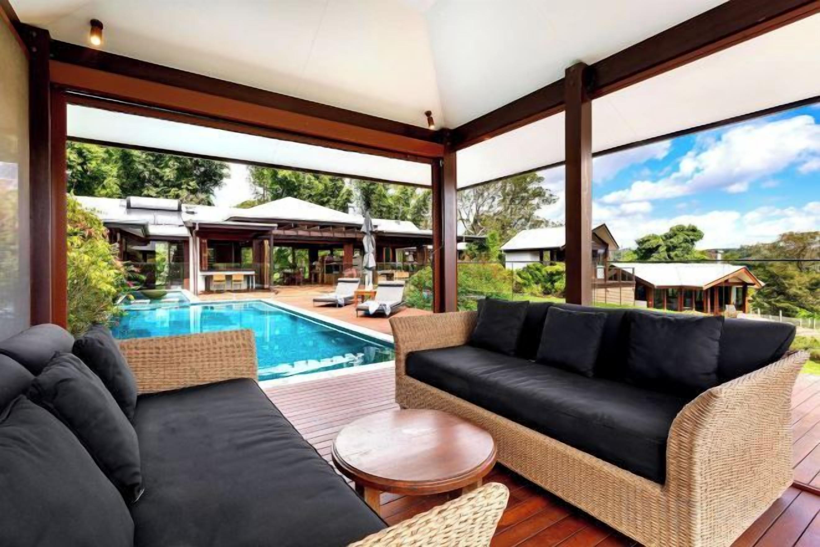 A spacious outdoor area with a pool, wicker furniture, and a view of a residential area.