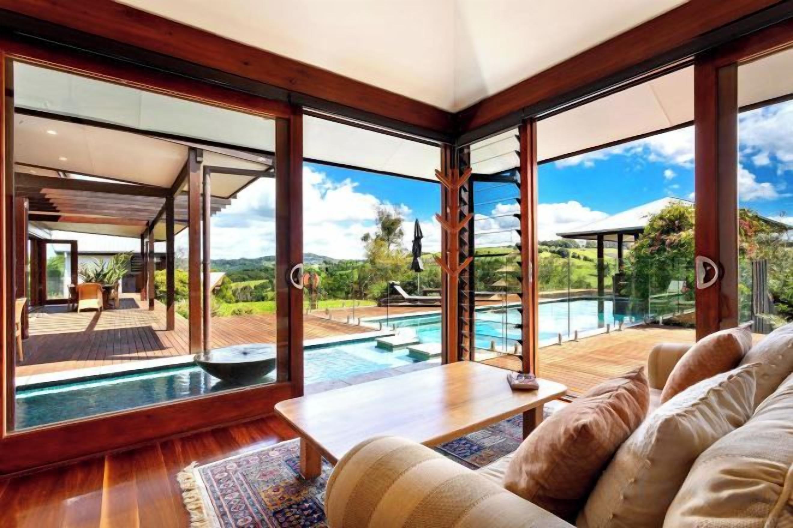 A room with a large sliding glass door leading to a pool area, a wooden floor, and a sofa with cushions.