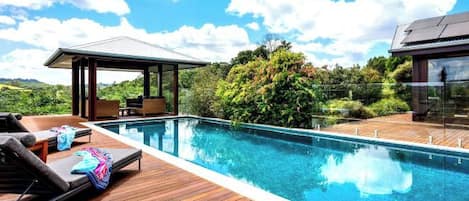 Un área junto a la piscina con sillones de descanso y una zona de estar techada.