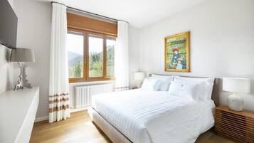 Habitación de hotel con una cama grande, una ventana con cortinas, un cuadro en la pared y una mesita de noche con lámpara.