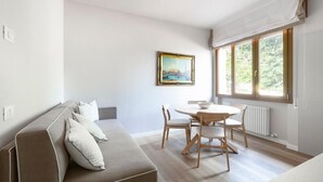 Una sala moderna con sofá, una mesa de comedor con sillas y un ventanal con vista a la vegetación.