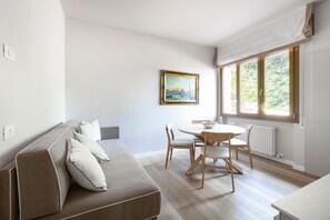 Una sala moderna con sofá, una mesa de comedor con sillas y un ventanal con vista a la vegetación.
