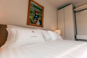 A hotel room with a bed, pillows, a painting, and a wardrobe.