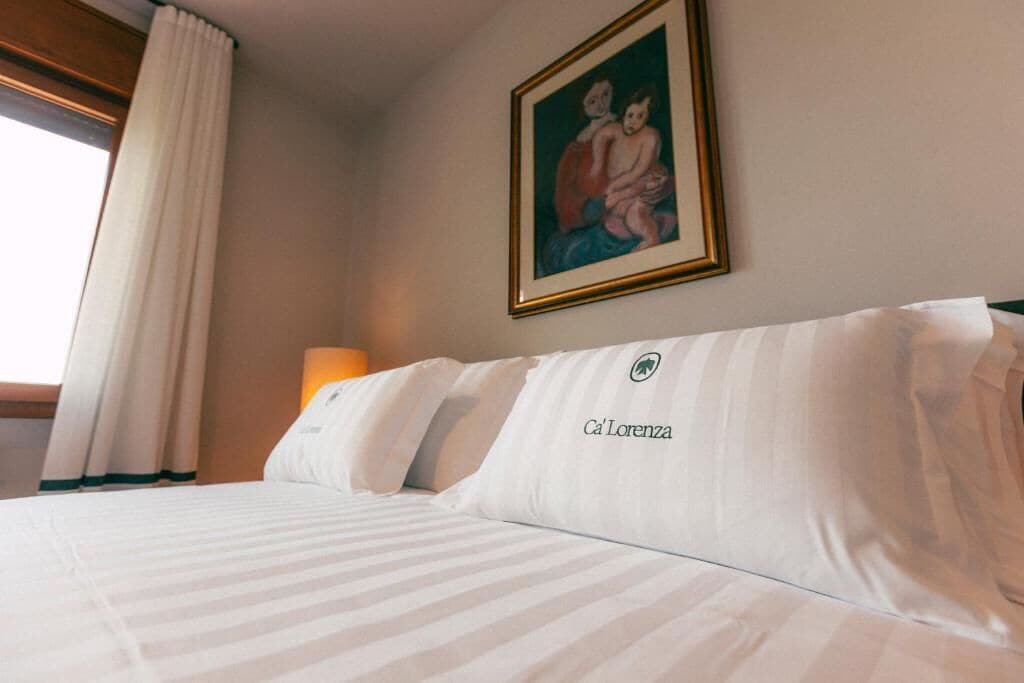 A hotel room with a bed, a painting on the wall, and a window with curtains.