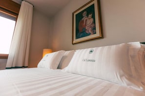 Una habitación de hotel con una cama, un cuadro en la pared y un ventanal con cortinas.
