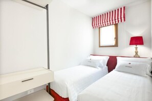 Habitación de hotel con dos camas, una mesita de noche, una ventana con cortina a rayas y una lámpara.