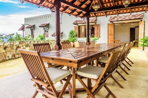 Un espacio de comedor al aire libre con una larga mesa de madera y sillas, rodeado de muros de piedra y plantas en macetas.