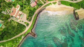 An aerial view of a coastal area with a sandy beach, a rocky shoreline, and a mix of residential buildings including a medical facility. - Cinnamon House, Weligama by The Serendipity Collection (Weligama)