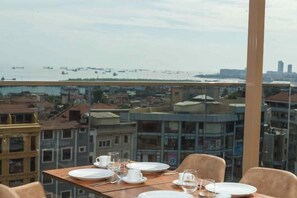 Taula de dinar arrebossada amb plats, gots i un got d'aigua, amb vista a un paisatge urbà ple d'edificis i embarcacions.