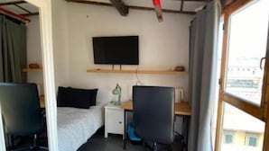 A small room with a bed, a desk, a chair, a TV, and a window.