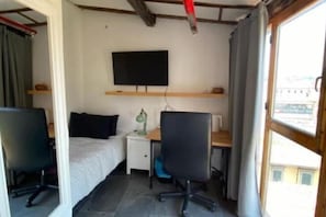 A small room with a bed, a desk, a chair, a TV, and a window.