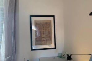 A framed map on a wall, a desk with a lamp, and a window with curtains.