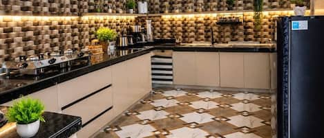 A modern kitchen with a patterned backsplash, a black refrigerator, and a tiled floor.