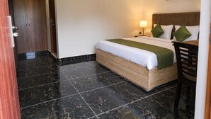 Habitación de hotel con cama, escritorio, silla, mesita de noche, lámpara y aire acondicionado instalado en la pared.