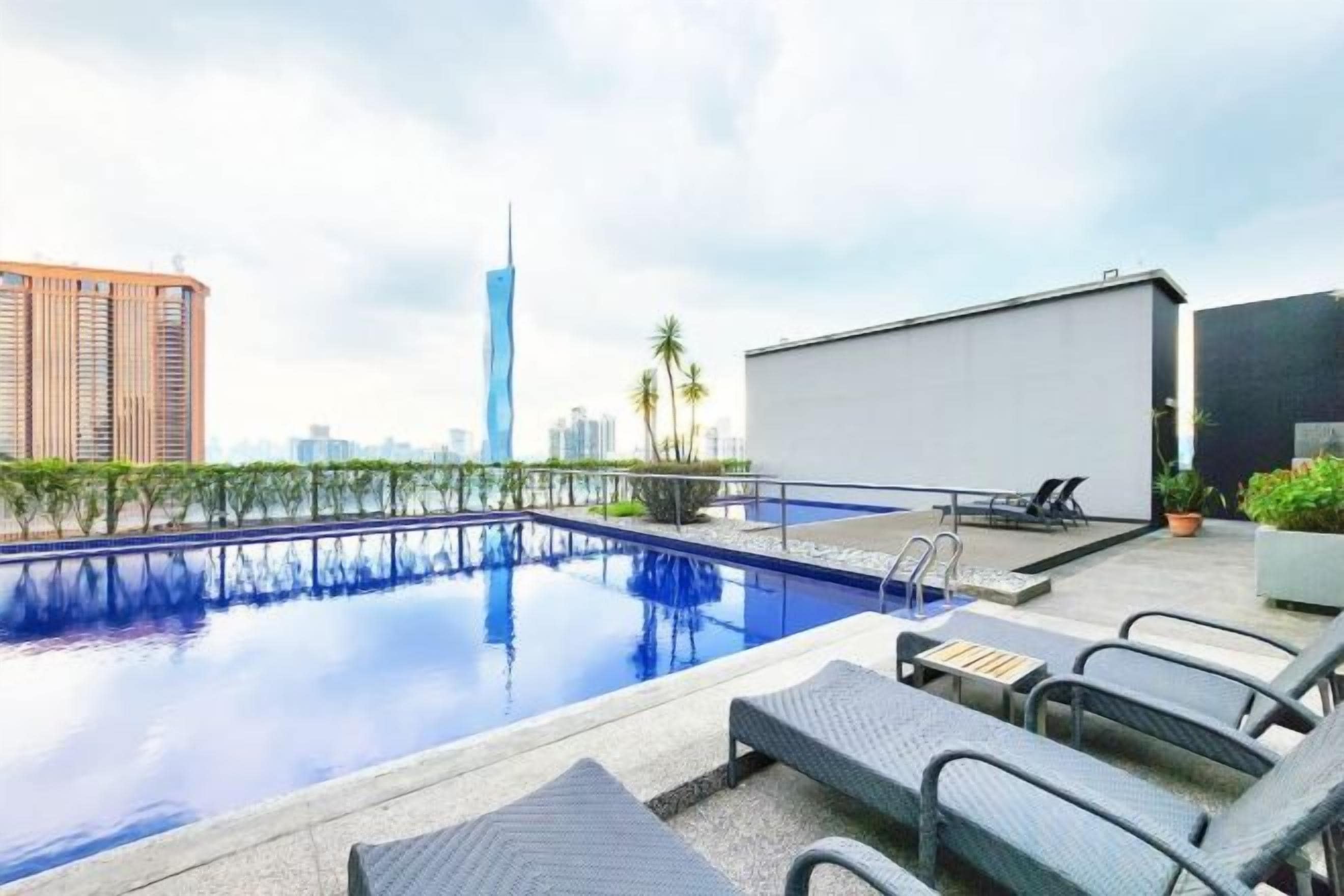 Ein Pool auf dem Dach mit Liegestühlen, einer Projektionsleinwand und einer Skyline im Hintergrund.