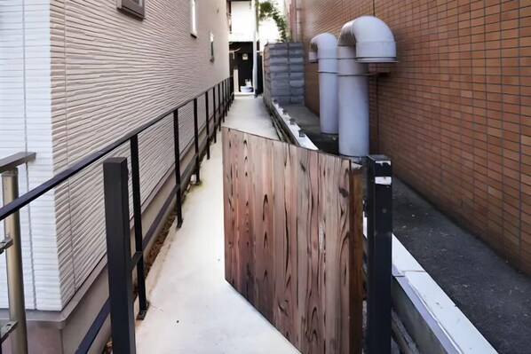 A narrow alleyway with a wooden fence, a metal railing, and a brick building on one side.