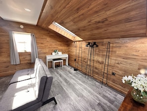 A room with a sloped ceiling, wooden walls, a piano, a sofa, a small table, and a coat rack.
