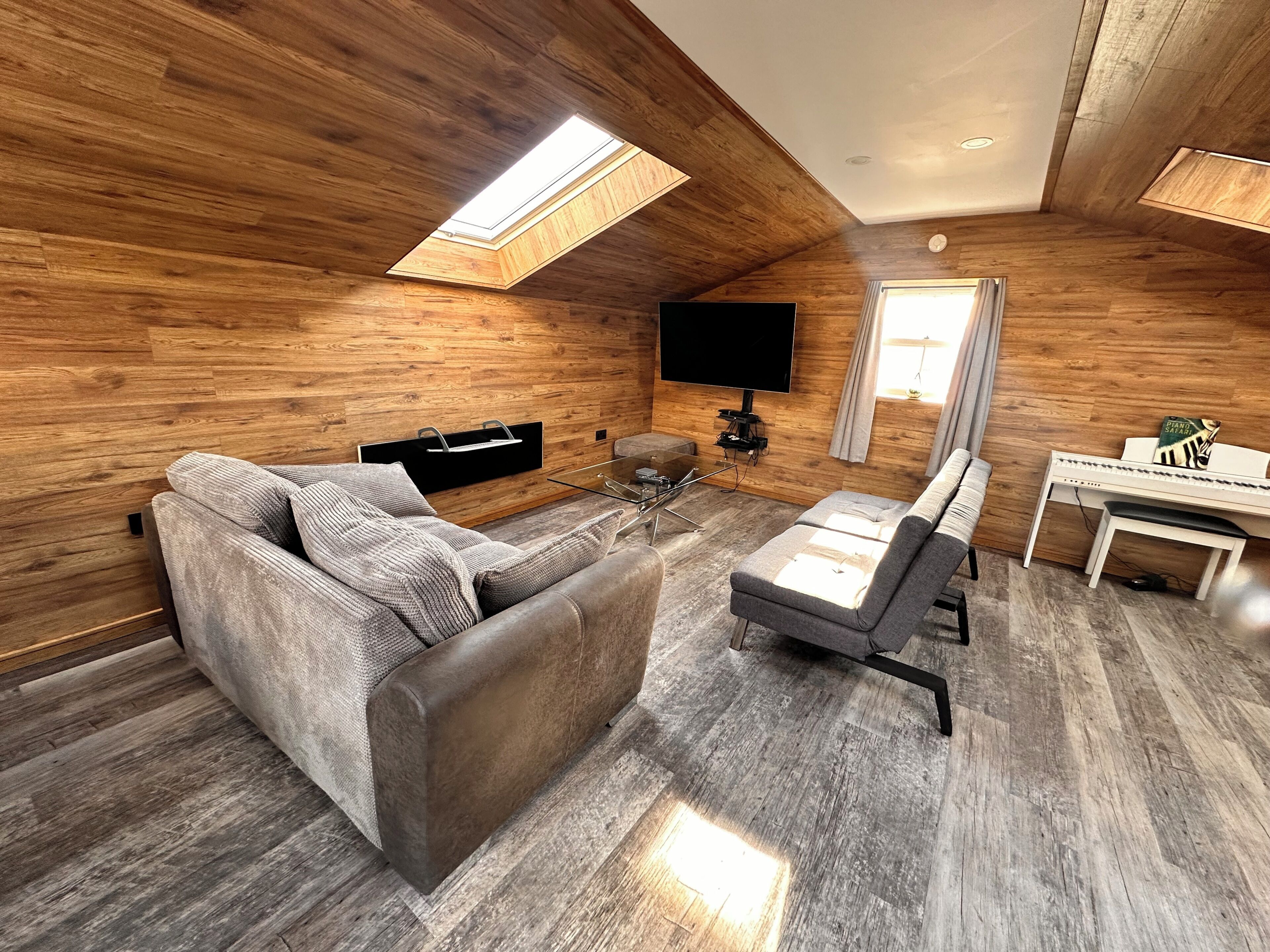 A modern living room with a sofa, a coffee table, a flat-screen TV, and a piano.