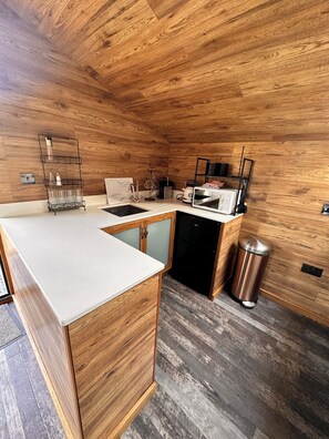 A modern kitchen with wooden cabinetry, a white countertop, and a black refrigerator.